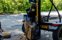 A FIRMAN Power Equipment 22-Ton Log Splitter machine outside, partially splitting a large wooden log, with green foliage in the background.