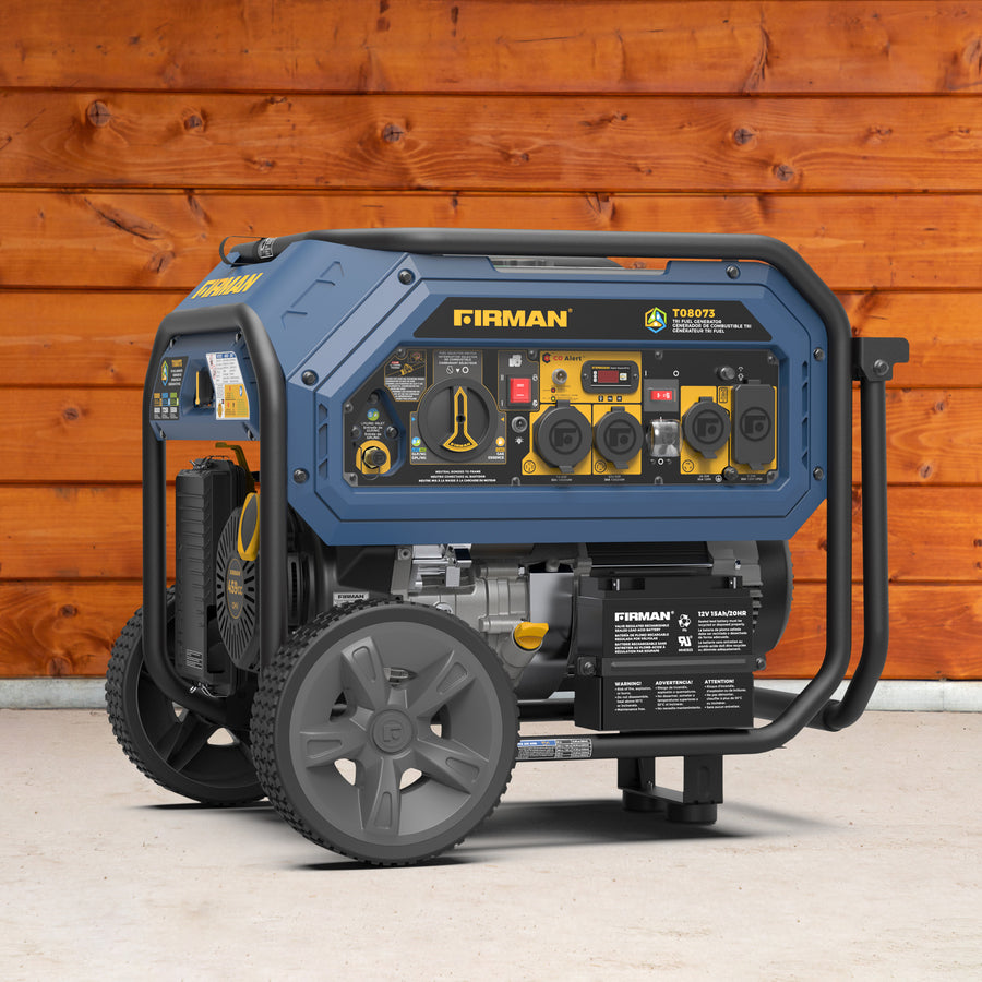 A FIRMAN tri-fuel portable generator with a blue frame and wheels sits on concrete in front of a wooden wall, offering 10,000 running watts (12,000 peak) and equipped with CO Alert technology for enhanced safety.