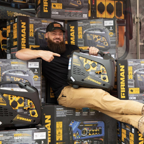 Image of a man sitting on FIRMAN Power Generator boxes and holding a small Inverter generator.