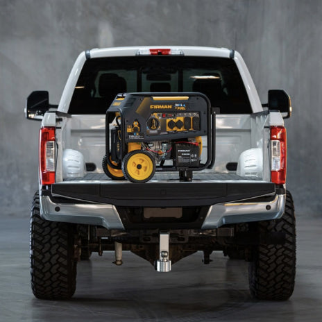 A FIRMAN generator is sitting on the bed of a white pick up truck. The truck is parked against a concrete wall.