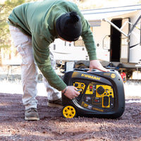 A person adjusts a FIRMAN Power Equipment Inverter Portable Generator 3300W Electric Start near a camper in a wooded campsite.
