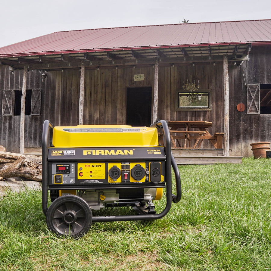 A Gas Portable Generator 4550W Recoil Start 120/240V with CO ALERT by FIRMAN Power Equipment in front of an old wooden barn with farming tools and a wooden table visible inside.