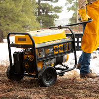 Person in yellow work pants standing beside a FIRMAN Power Equipment Gas Portable Generator 7125W Recoil Start 120/240V on a forest ground.