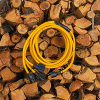 A coiled yellow FIRMAN Power Equipment heavy-duty power cord with black connectors rests on a pile of cut wooden logs.
