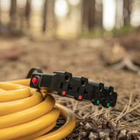A yellow FIRMAN Power Equipment coiled garden hose with a black multi-setting nozzle lying on a forest floor covered in pine needles.