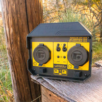 A yellow and black FIRMAN Power Equipment 50A PORTABLE GENERATOR PARALLEL KIT rests outdoors near a wooden post, surrounded by grass and trees—perfect for connecting inverter generators for RV-ready power.