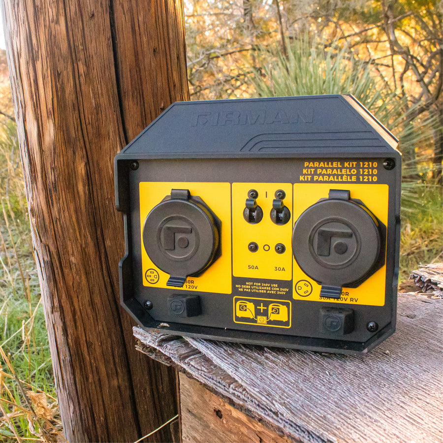 A yellow and black FIRMAN Power Equipment 50A PORTABLE GENERATOR PARALLEL KIT rests outdoors near a wooden post, surrounded by grass and trees—perfect for connecting inverter generators for RV-ready power.
