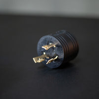 A black, three-pronged FIRMAN Power Equipment generator plug lying on a dark surface, displaying the electrical connectors.