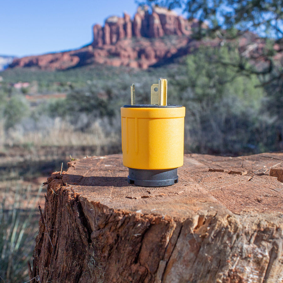 Yellow FIRMAN Power Equipment TT-30P to L5-30R Adapter electrical plug on a tree stump with a scenic desert mountainscape in the background.
