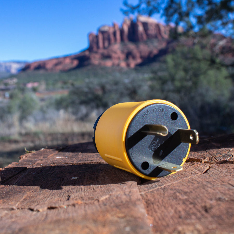 A portable yellow stove placed on a wooden surface with a scenic mountainous backdrop, featuring a FIRMAN Power Equipment TT-30P to L5-30R adapter.