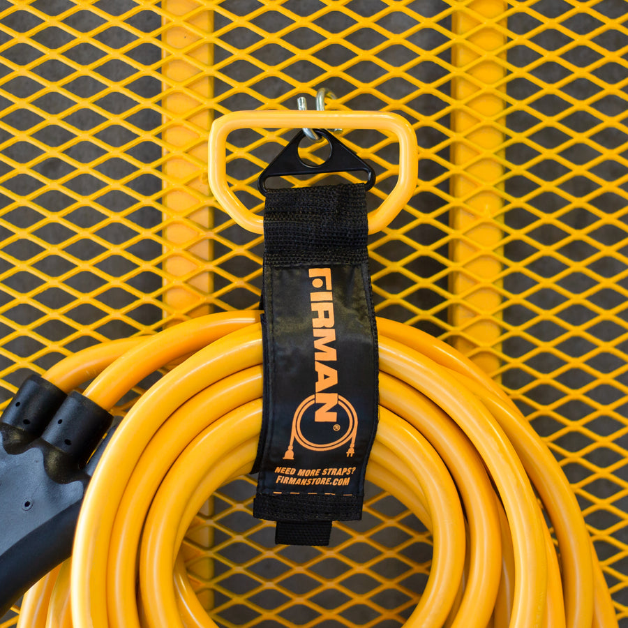 A yellow extension cord neatly coiled and hung on a yellow metal grid wall, secured with a Heavy Duty Storage Strap With Handle labeled "FIRMAN Power Equipment.