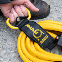 A person's hand holding a yellow extension cord secured with a FIRMAN Power Equipment Heavy Duty Storage Strap With Handle near their boot on a concrete surface.