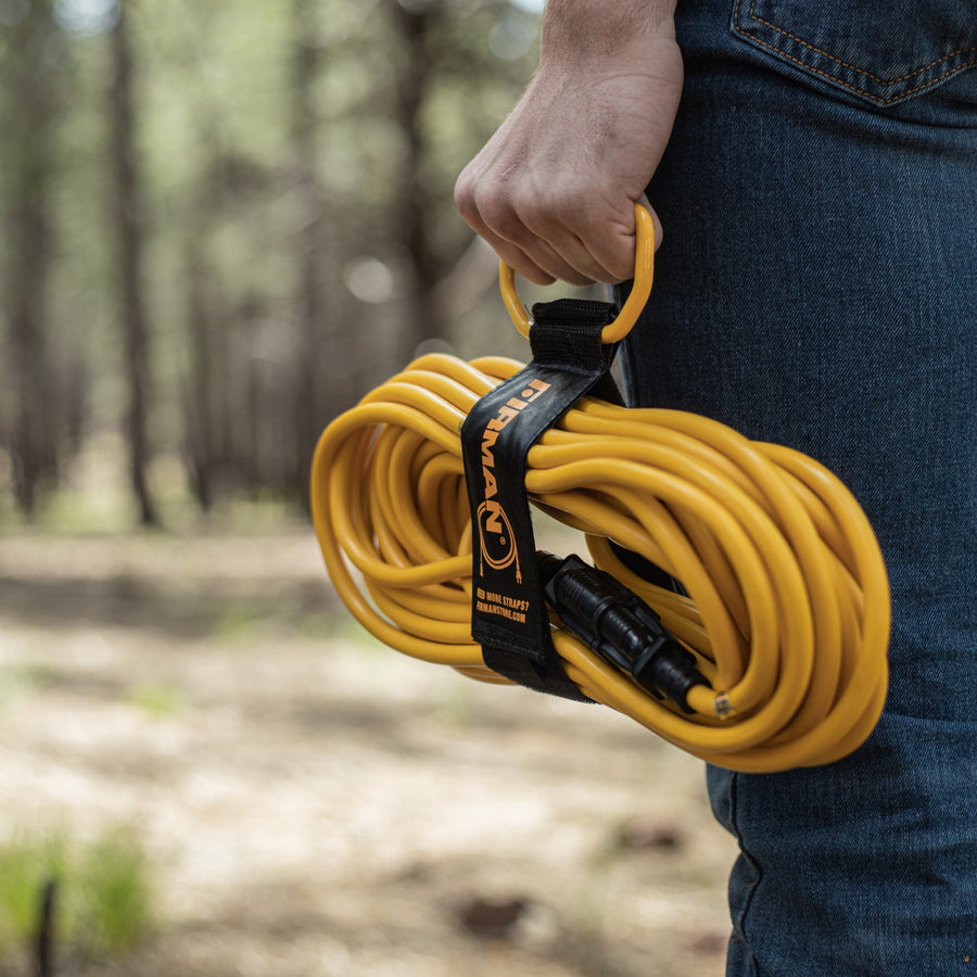 A person outdoors holds the FIRMAN Power Equipment 50ft Medium Duty 5-15P to 5-15R Generator Utility Power Cord with Storage Strap, ready to use this durable extension cord for any power task.