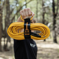 A person holds a 50ft Medium Duty 5-15P to 5-15R Generator Utility Power Cord with Storage Strap by FIRMAN Power Equipment outdoors in a wooded area.