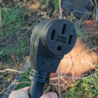A hand holding a frost-covered FIRMAN Power Equipment 50A Parallel Cord Kit outdoors, with grass and leaves in the background.
