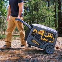 A person wearing a black shirt and tan pants wheels a FIRMAN Power Equipment Gas Inverter Portable Generator 6650/5300 Watt 120/240V CO Alert along a dirt path in an outdoor, wooded area.