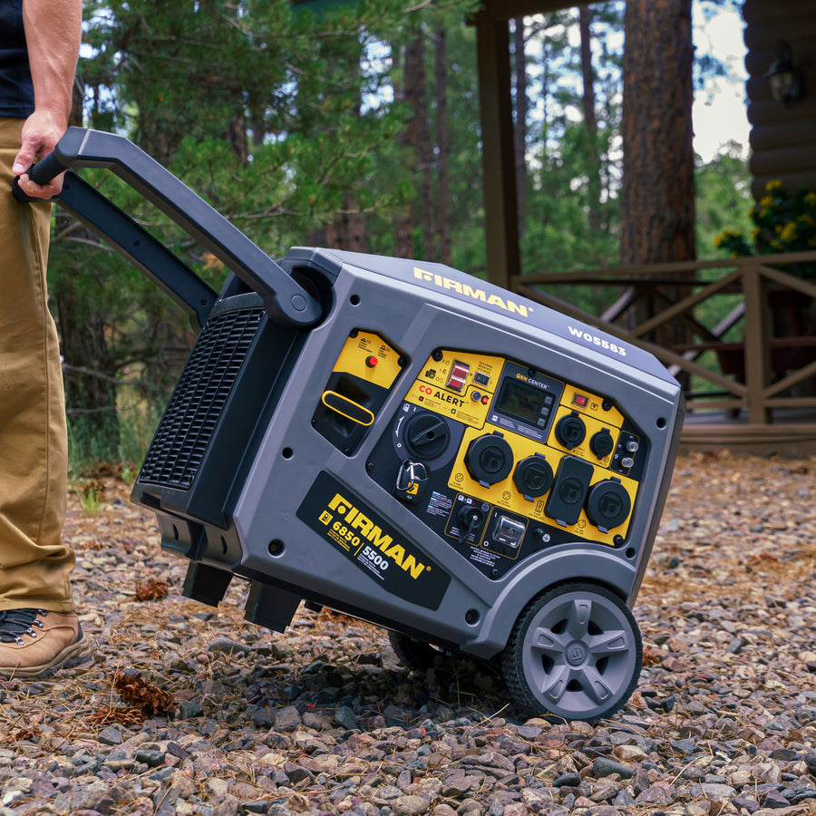 A person is pulling a FIRMAN Power Equipment Gas Inverter Portable Generator 6850/5500 Watt Remote Start 120/240V CO Alert on a rough gravel surface near a wooden cabin surrounded by trees, ready to engage the eco mode for quieter operation.