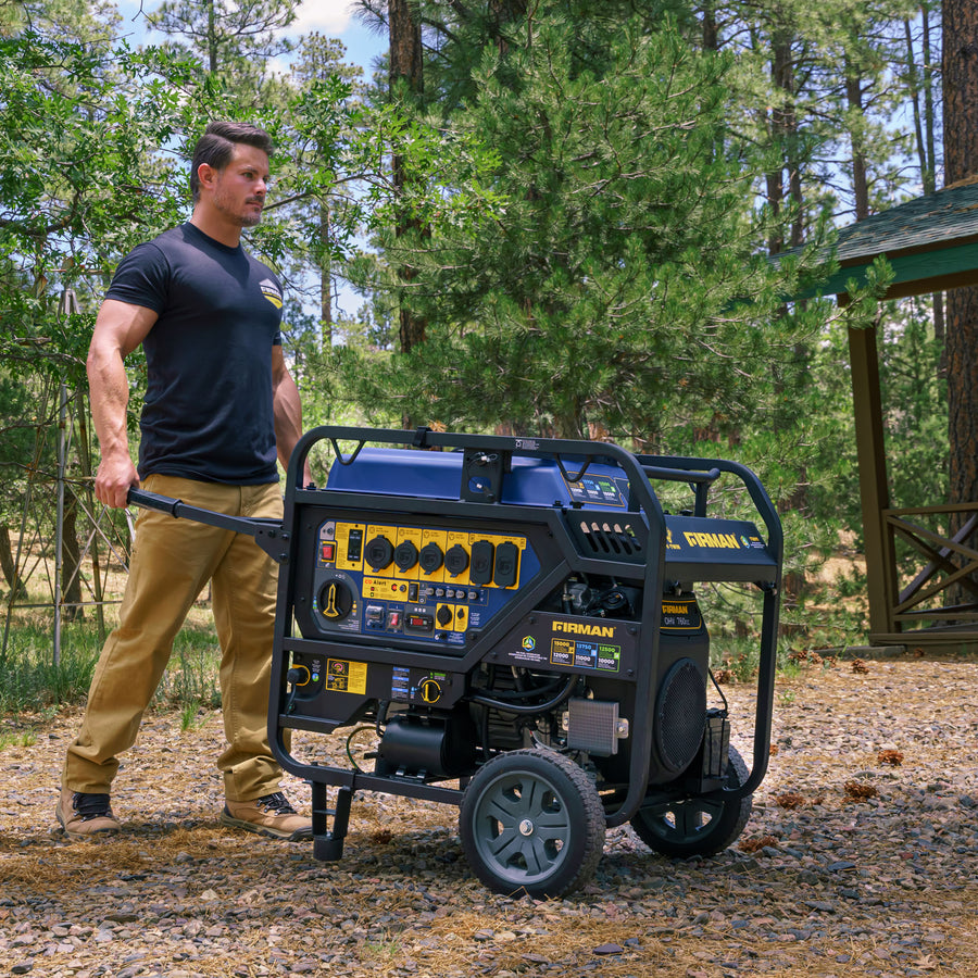 A man stands next to a large, black TRI FUEL PORTABLE GENERATOR 15000W ELECTRIC START 120/240V WITH CO ALERT by FIRMAN Power Equipment outdoors with trees and a cabin in the background.