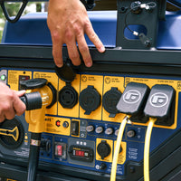 A person plugs a yellow power cable into the blue and yellow generator control panel, featuring various switches, sockets, and meters on the robust 15000-watt TRI FUEL PORTABLE GENERATOR 15000W ELECTRIC START 120/240V WITH CO ALERT by FIRMAN Power Equipment.