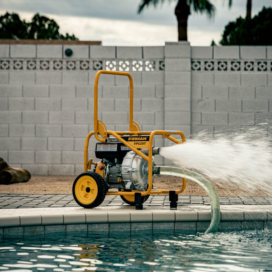 A portable 2-Inch Portable High Pressure Water and Semi-Trash Pump by FIRMAN Power Equipment, featuring a vibrant yellow frame, efficiently pumps water into a swimming pool in a backyard setting. This gas-powered, self-priming cast iron pump is designed for easy and effective use.