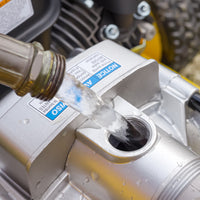 Water is poured from a hose into the metal opening of a FIRMAN Power Equipment 2-Inch Portable High Pressure Water and Semi-Trash Pump, with instruction labels visible on the surface.