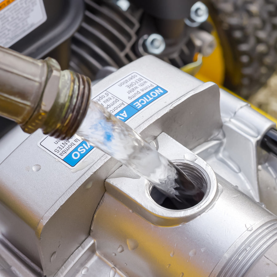 Water is poured from a hose into the metal opening of a FIRMAN Power Equipment 2-Inch Portable High Pressure Water and Semi-Trash Pump, with instruction labels visible on the surface.