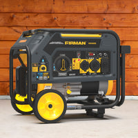 A FIRMAN Power Equipment Dual Fuel Portable Generator 4550/3650W Recoil Start with control panel, wheels, and handle sits on a concrete floor by a wooden wall, providing dependable energy wherever needed.