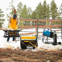 A person wearing a welding helmet and gloves using an angle grinder on a metal fence in a snowy environment, with a FIRMAN Power Equipment Gas Portable Generator 4450W Recoil Start 120V with CO alert nearby.