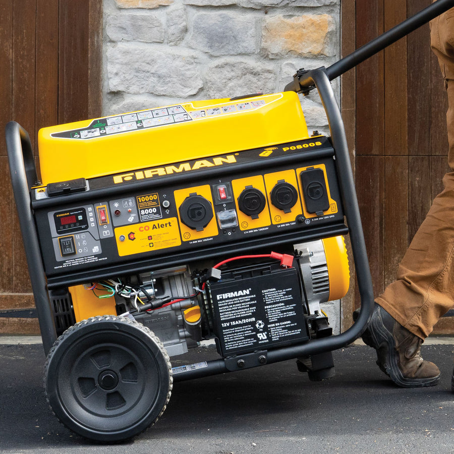 A person moves a yellow FIRMAN Power Equipment Gas Portable Generator 10000W Remote Start 120/240V with CO Alert on wheels outdoors near a stone and wood wall.