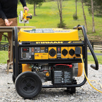 A yellow FIRMAN Power Equipment Gas Portable Generator 10000W Remote Start 120/240V with CO Alert runs on gravel outdoors, powering a tool via extension cord as someone works at a nearby table.