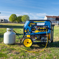 A FIRMAN Power Equipment Tri Fuel 8000W Portable Generator Electric Start 120/240V with CO ALERT is placed outdoors on grass next to a propane tank, cables attached, with buildings and trees in the background.