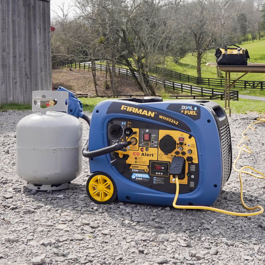 Blue FIRMAN Power Equipment RV-ready dual-fuel generator connected to a propane tank, situated on a gravel surface with greenery and picnic tables in the background.