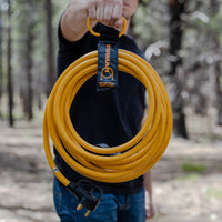 A man holding a coiled yellow FIRMAN Power Equipment 25' Heavy Duty TT-30P to TT-30R Power Cord With Storage Strap.
