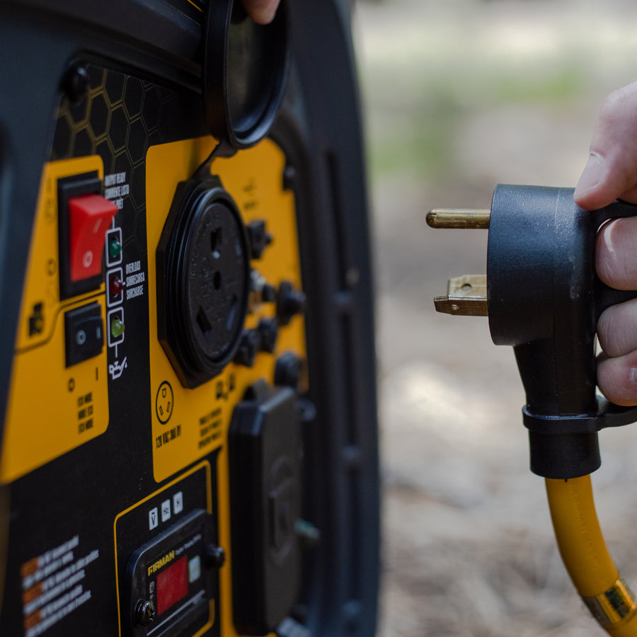 A person's hand plugging a FIRMAN Power Equipment 25' Heavy Duty TT-30P to TT-30R Power Cord With Storage Strap into a portable generator in an outdoor setting.