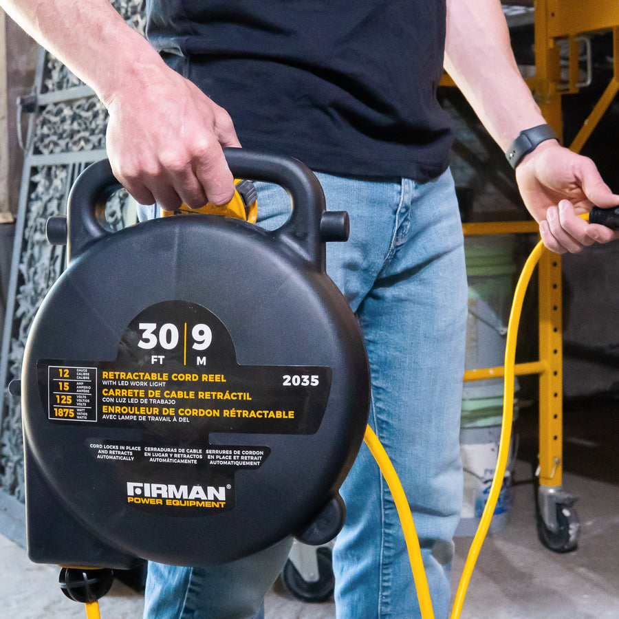 A person holding a FIRMAN Power Equipment retractable extension cord reel in a workshop, partially unwinding a yellow electrical cable.