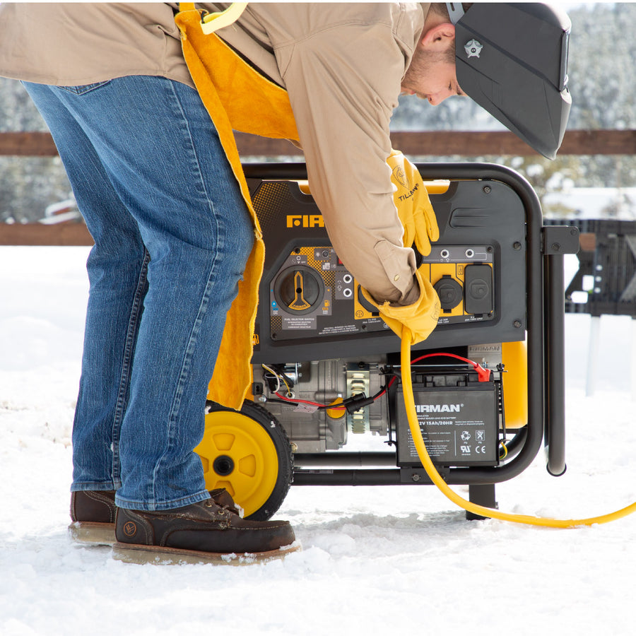 A person in jeans and a jacket using a FIRMAN Power Equipment Dual Fuel Portable Generator 8000W Electric Start 120/240V in a snowy environment.
