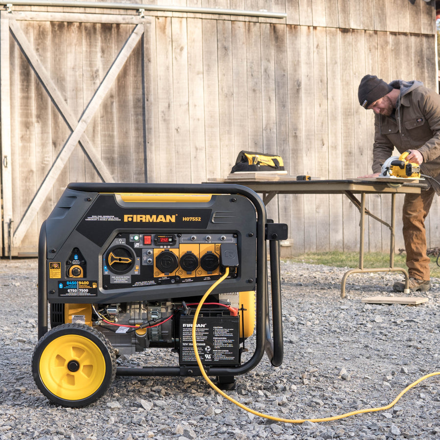 A man in a beanie using a power tool at a work table outdoors near a FIRMAN Power Equipment Dual Fuel Portable Generator 7500W Electric Start 120/240V.