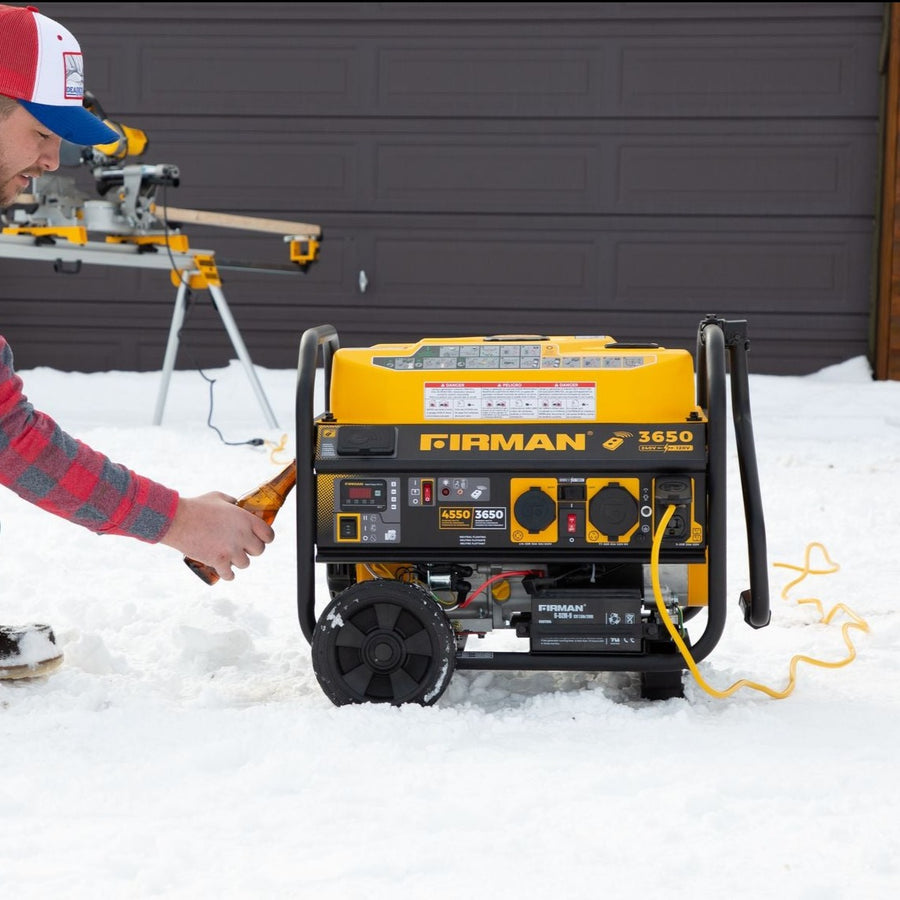 Man in a red plaid shirt and cap starts a FIRMAN Power Equipment Gas Portable Generator 4550W Remote Start 120/240V as backup power in the snow outside a garage.