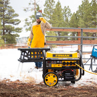 Man in yellow apron adjusts a FIRMAN Power Equipment Gas Portable Generator 11400W Remote Start 120/240V with CO alert in a snowy outdoor setting.