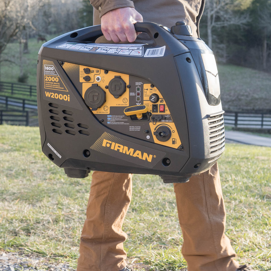 A person holding a FIRMAN Power Equipment Refurbished Gas Inverter 2000W Recoil Start outdoors during daylight.