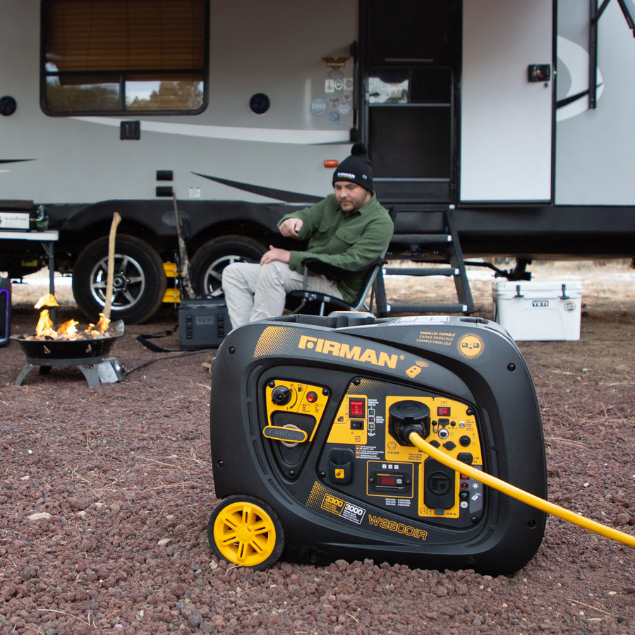 Man sitting outside an RV near a FIRMAN Power Equipment Inverter Portable Generator 3300W Remote Start and a small campfire, in a camping area with gravel ground.