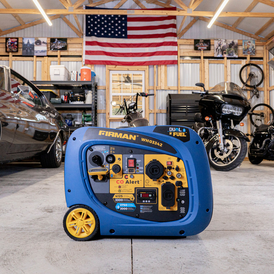 A FIRMAN Dual Fuel Inverter Portable Generator 4125W Electric Start with CO ALERT from the Whisper Series is in a garage, with cars and motorcycles in the background, and an American flag hanging on the wall.